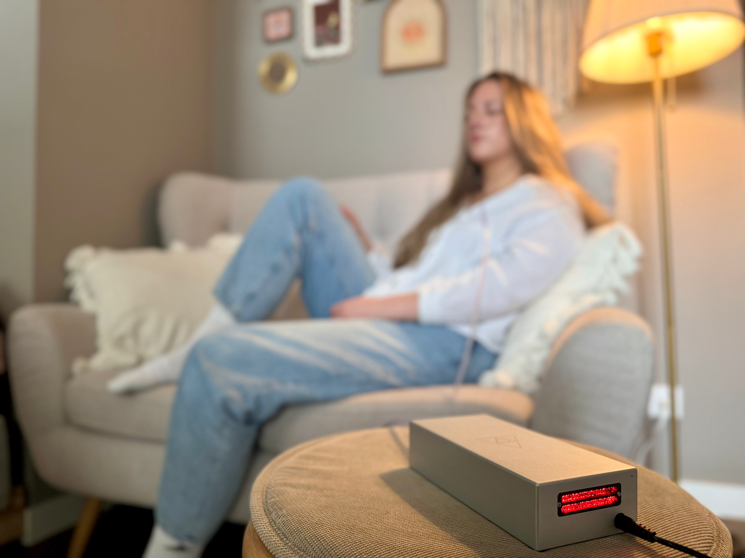 Woman in an armchair beside a floor lamp, the device on the stool