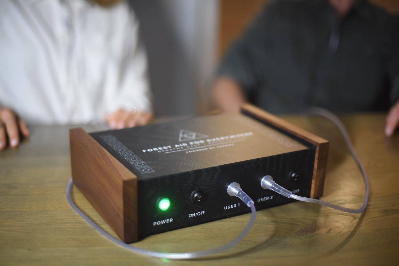 A Forest Air device on a wooden table, two people sitting behind it
